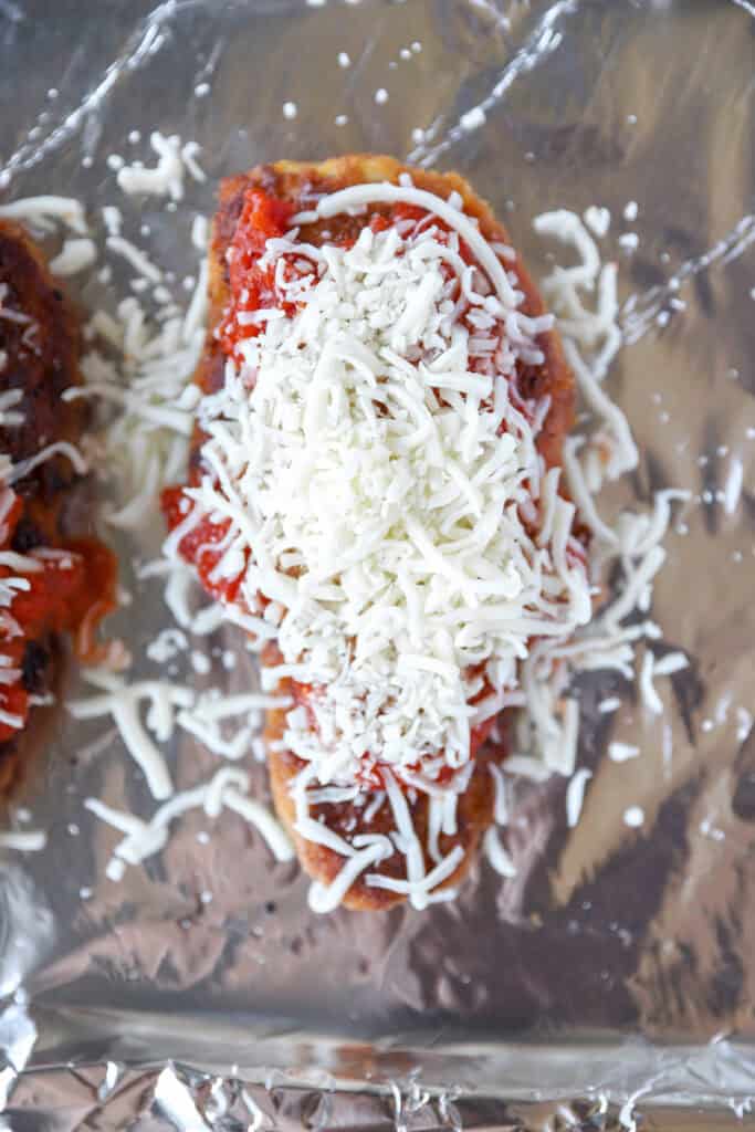 overhead photo of the chicken on foil topped with marinara sauce and cheese.