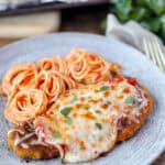 spicy chicken parm on a grey plate with swirled spaghetti.