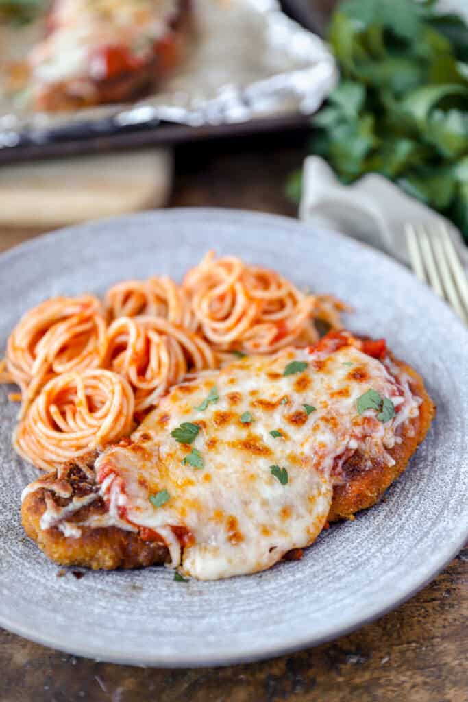 spicy chicken parm on a grey plate with swirled spaghetti.