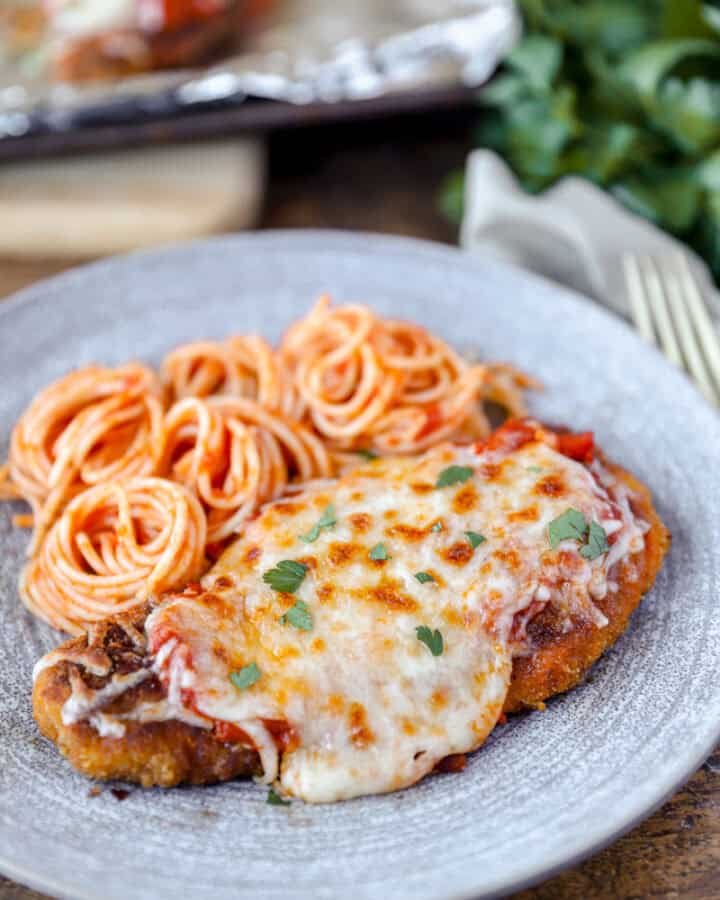 spicy chicken parm on a grey plate with swirled spaghetti.