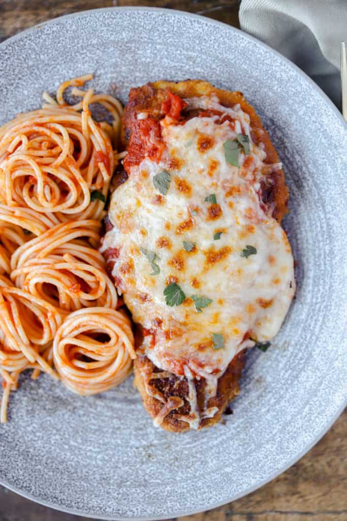 overhead photo of the spicy chicken  parm on a grey plate with swirled spaghetti.