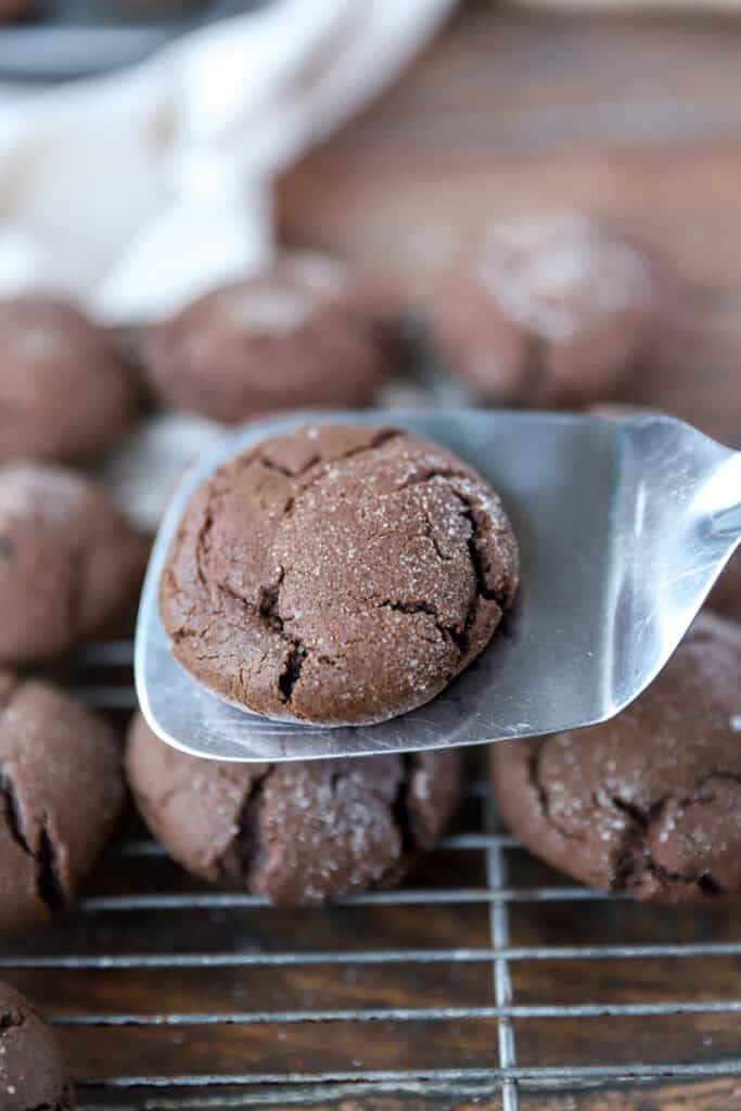 a spatula scooping a chocolate espresso snickerdoodle to a cooling rack with more cookies.