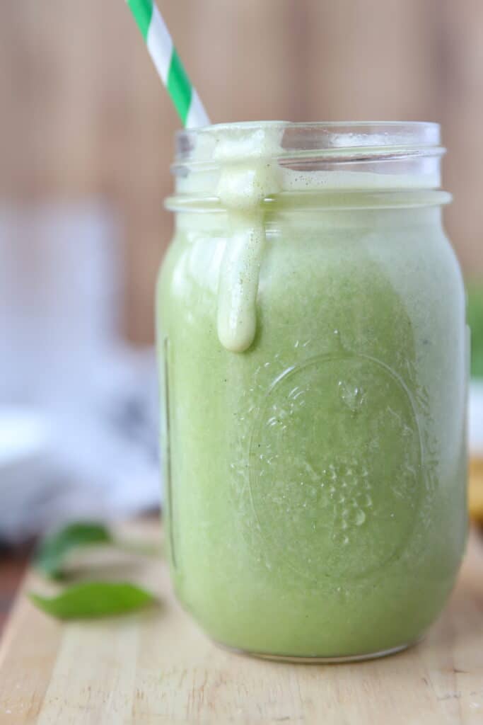 banana spinach smooth in a mason jar glass with a green and white striped straw.