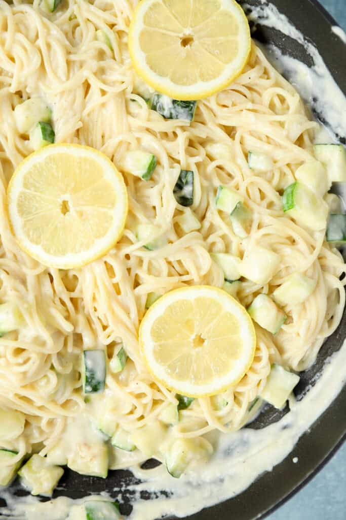 overhead photo of lemon zucchini pasta topped with lemon slices in a nonstick pan.