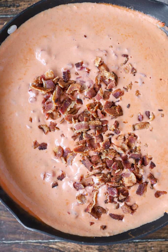 overhead photo of the tomato sauce in the nonstick pan now with the crumbled bacon pieces on top of the sauce.