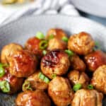 chicken teriyaki meatballs topped with diced scallions in a round grey bowl.