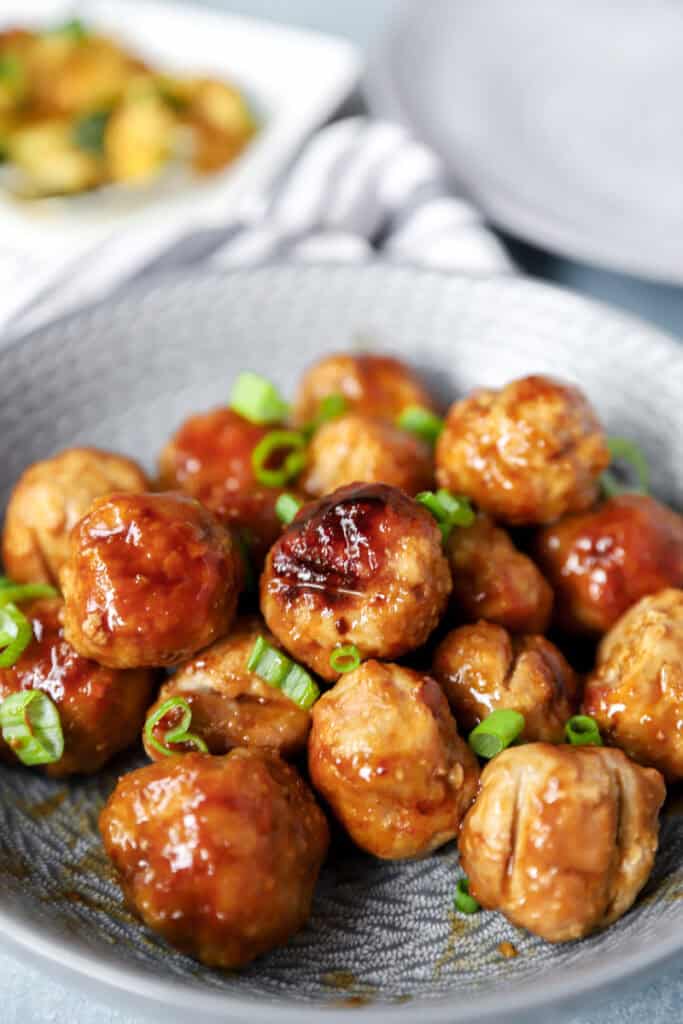 chicken teriyaki meatballs topped with diced scallions in a round grey bowl.