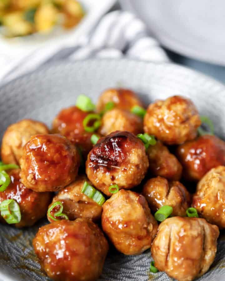 chicken teriyaki meatballs topped with diced scallions in a round grey bowl.