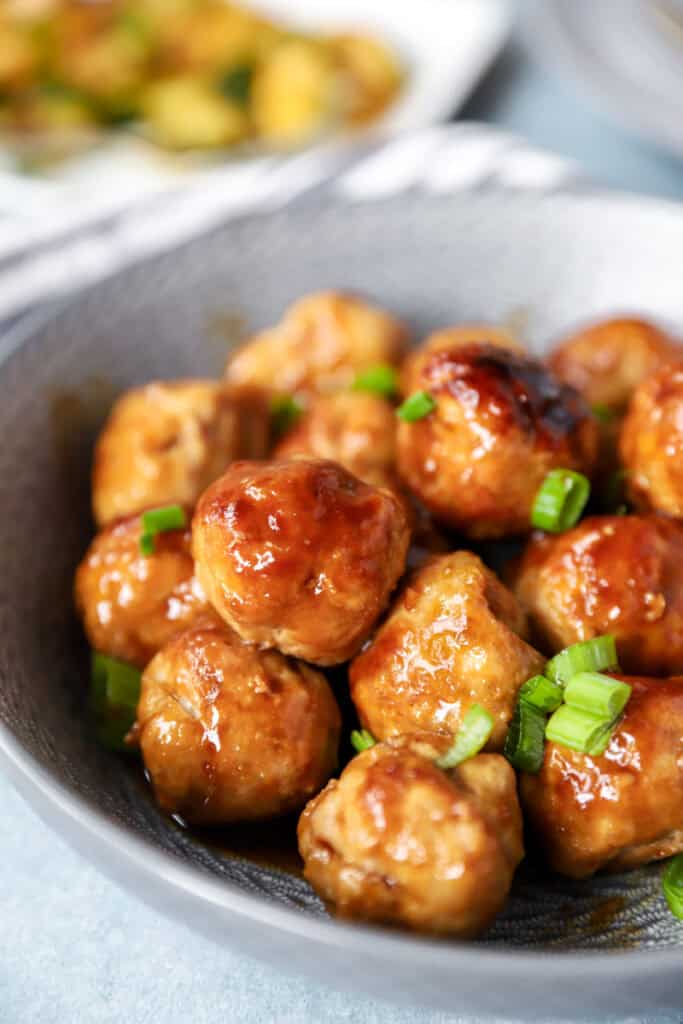 a pile of the chicken teriyaki meatballs topped with diced scallions in a round grey bowl.
