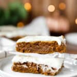 stack of 2 iced pumpkin cookie bars on a stack of small round white plates.
