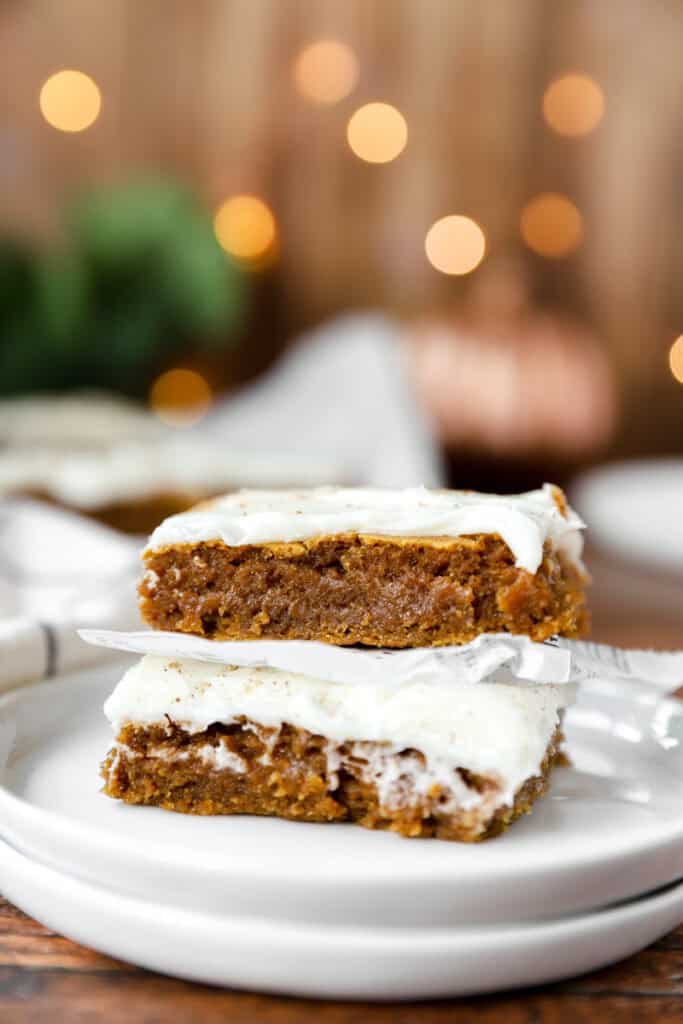 stack of 2 iced pumpkin cookie bars on a stack of small round white plates.