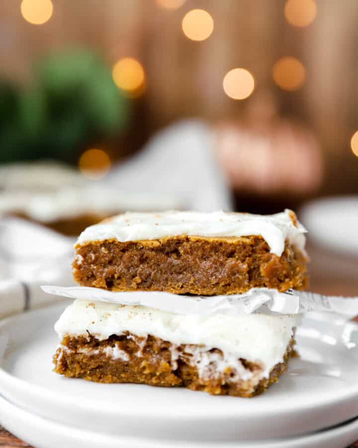 stack of 2 iced pumpkin cookie bars on a stack of small round white plates.