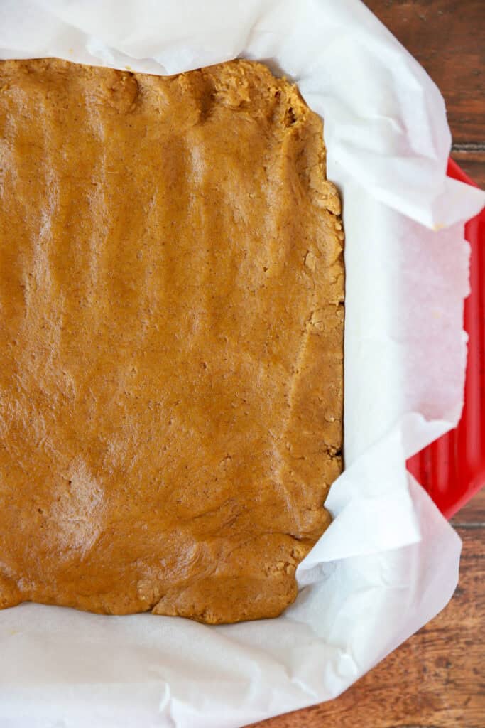 overhead photo of the pumpkin cookie dough pressed into a parchment paper lined 8x8 baking dish.