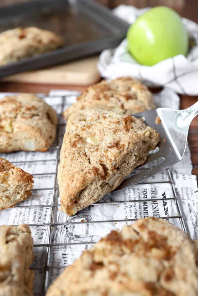 a spatula placing one of the apple cinnamon scones on a baking rack.