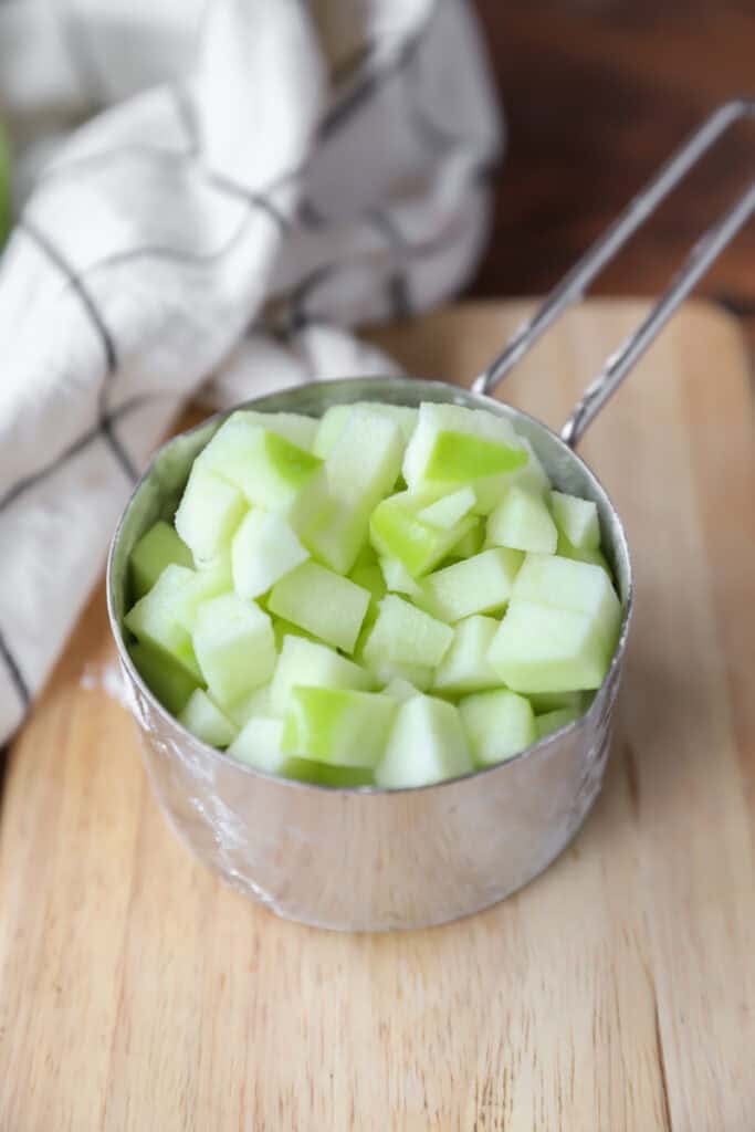 diced granny smith apples in a silver measuring cup.