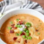 creamy tortellini soup topped with bacon and peas in a round white bowl.