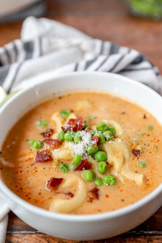 creamy tortellini soup topped with bacon and peas in a round white bowl.